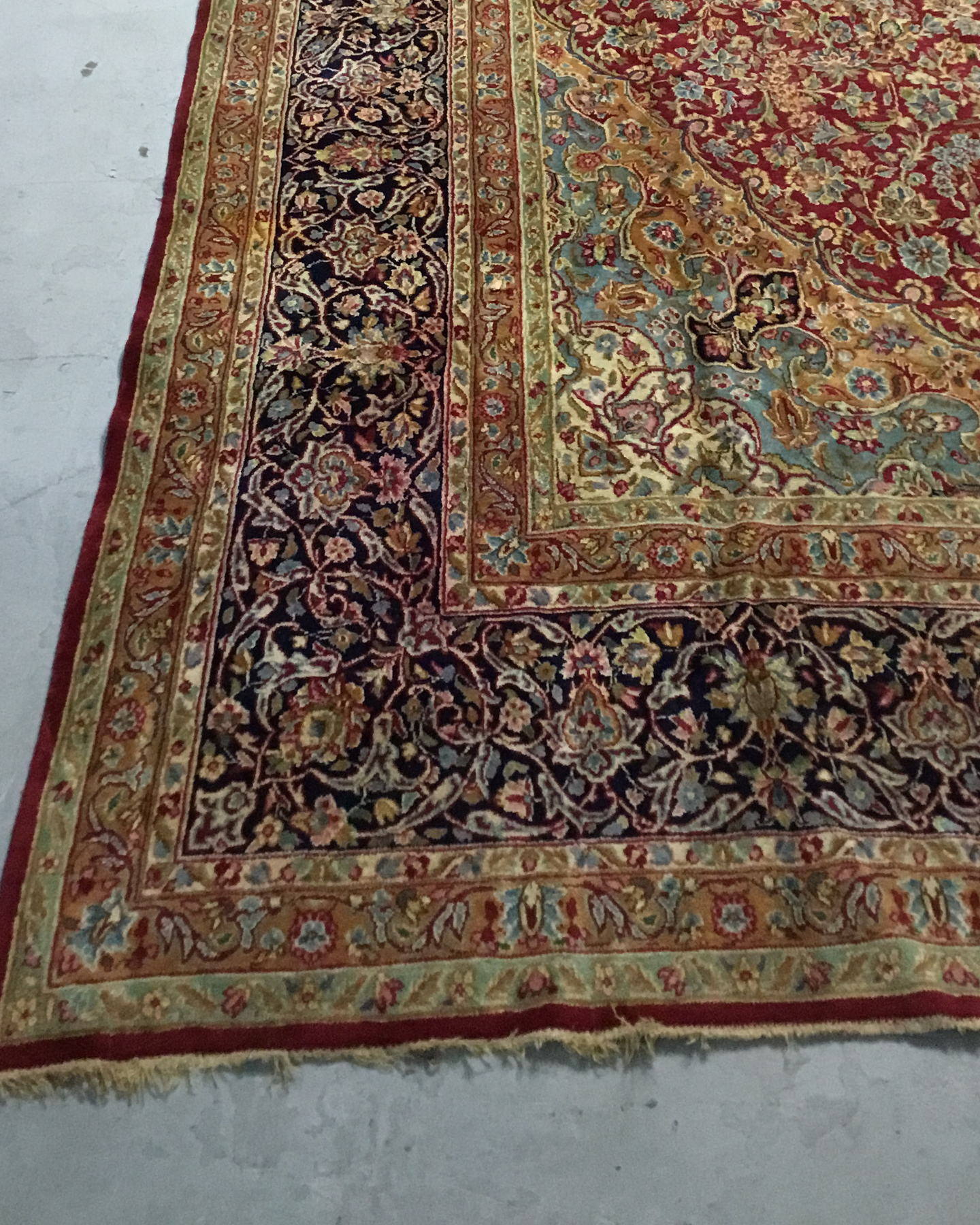 Corner of the same rug before cleaning, the navy border and ivory fringe dulled and flattened in tone